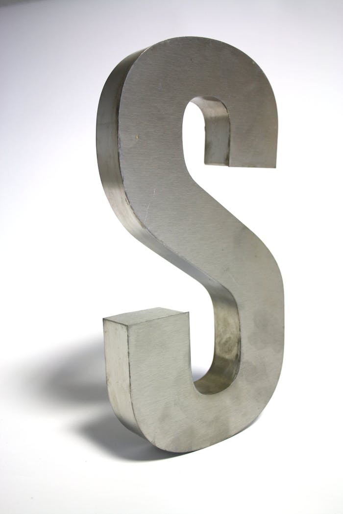 Close-up of a metallic letter S sculpture made of silver iron on a white background.